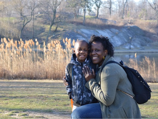 Una madre negra y su hijo se abrazan afuera en un parque. Hace frío y llevan abrigos de invierno.