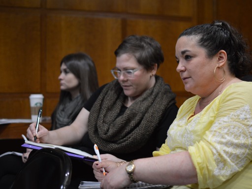 Tres mujeres se sientan en una sala de conferencias tomando notas. Están muy atentas.