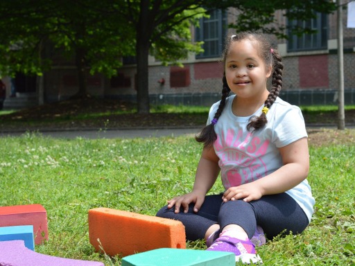 Una niña con discapacidad se sienta en un parque con juguetes coloridos a su alrededor.